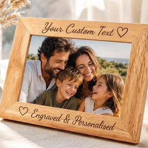 Könnte beinhalten: Ein rechteckiger Bilderrahmen aus hellem Holz mit natürlicher Maserung. Der obere Rand ist mit dem Text "Your Custom Text" und einem Herzsymbol graviert. Der untere Rand zeigt ein Herzsymbol und den Text "Engraved & Personalised".