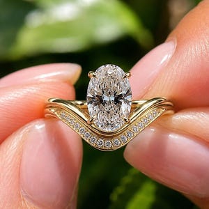 Peut inclure: Une bague en or composée d'une pierre centrale transparente taille ovale fixée par quatre griffes, accompagnée d'un anneau incurvé orné d'une rangée de petites pierres transparentes rondes. Le métal présente une finition jaune polie.