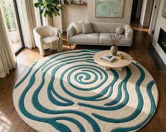 May include: A round area rug with a cream-colored background and a teal wave pattern. The rug is centered in a living room with hardwood floors, a sofa, and a coffee table. The rug's design features a spiral in the center.