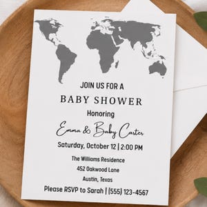 May include: A white rectangular baby shower invitation card featuring a grey world map graphic at the top. The text reads: JOIN US FOR A BABY SHOWER Honoring Emma & Baby Carter Saturday, October 12 | 2:00 PM The Williams Residence 452 Oakwood Lane Austin, Texas Please RSVP to Sarah | (555) 123-4567.