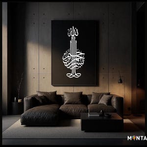 Op de afbeelding: Een groot zwart canvas met witte Arabische kalligrafie hangt boven een donkerbruine hoekbank. De kamer heeft een modern, minimalistisch design met donkere muren en een lage salontafel. De woorden "Dark & Bold" staan verticaal afgedrukt.