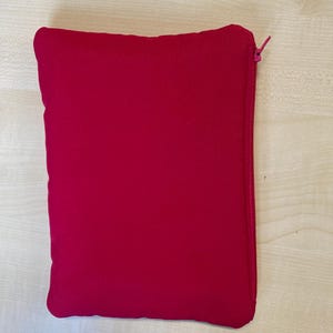 May include: A rectangular, magenta-colored pouch with a zipper closure. The pouch is made of a soft, possibly felt-like material. The zipper is a matching magenta color.