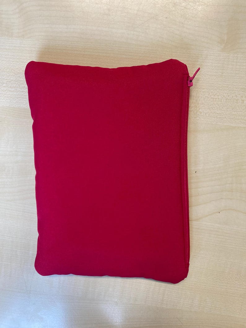 May include: A rectangular, magenta-colored pouch with a zipper closure. The pouch is made of a soft, possibly felt-like material. The zipper is a matching magenta color.