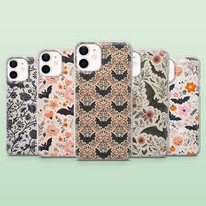 May include: A collection of five phone cases with various Halloween-themed designs. The cases feature floral patterns, bats, pumpkins, and other spooky elements in colors like black, orange, pink, and cream. The cases are made of clear plastic.