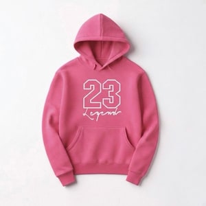Puede incluir: Sudadera con capucha rosa con bolsillo delantero. El n&uacute;mero "23" en blanco, con tipograf&iacute;a universitaria, y la palabra "Legend" debajo en cursiva. La sudadera con capucha est&aacute; hecha de un material suave.