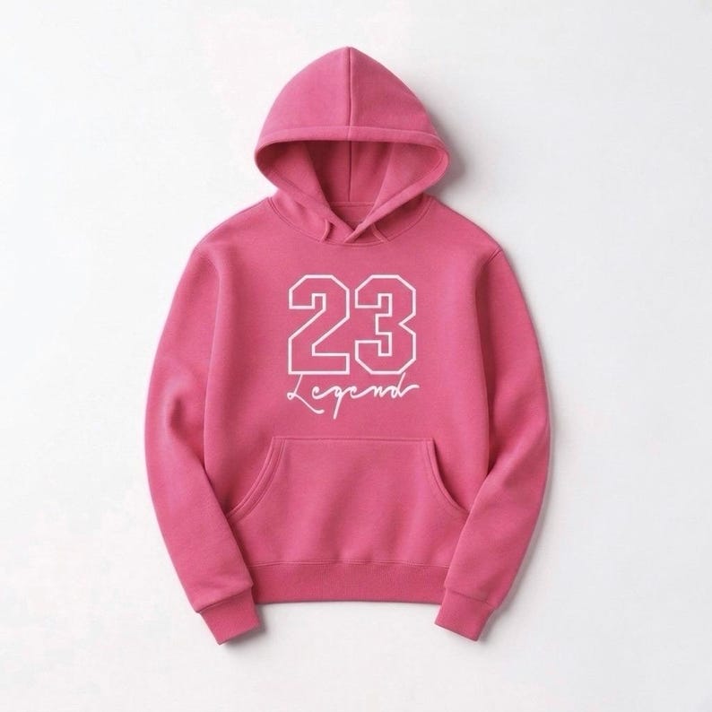 Puede incluir: Sudadera con capucha rosa con bolsillo delantero. El n&uacute;mero "23" en blanco, con tipograf&iacute;a universitaria, y la palabra "Legend" debajo en cursiva. La sudadera con capucha est&aacute; hecha de un material suave.