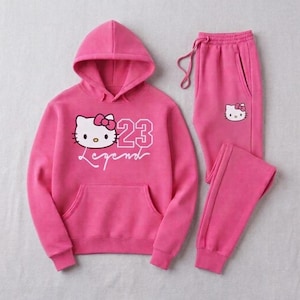 Pu&ograve; includere: Un completo tuta rosa acceso composto da una felpa con cappuccio e pantaloni abbinati. La felpa con cappuccio presenta una grafica di un gatto dei cartoni animati, il numero 23 e la parola "Legend". Anche i pantaloni hanno una piccola grafica di gatto.