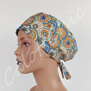 Peut inclure: Une charlotte de bloc opératoire arborant un motif répétitif de fleurs stylisées et de cercles dans des tons orange, bleu, jaune et blanc. Ce couvre-chef en tissu présente une calotte arrondie et se noue à l'arrière pour un ajustement sûr.