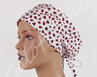 May include: A white scrub cap featuring a repeating pattern of small red and black ladybugs. The cap is designed with a tie-back closure at the nape of the neck, allowing for an adjustable fit. The fabric is lightweight and covers the head.