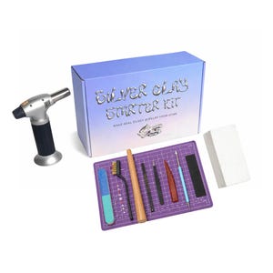 May include: A silver clay starter kit with a blue and silver box, a small torch, and various tools. The kit includes a purple cutting mat, a sanding block, brushes, and other jewelry-making tools. The box reads "Silver Clay Starter Kit".