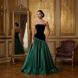 Könnte beinhalten: Ein trägerloses Abendkleid mit einem schwarzen Samtkorsett und einem fließenden smaragdgrünen Rock. Das Kleid wird in einem Raum mit einem großen goldenen Spiegel und einem Vintage-Stuhl getragen.