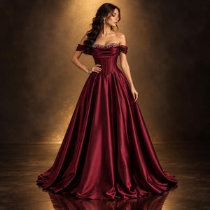 May include: A floor-length, off-the-shoulder gown in a deep burgundy satin fabric. The bodice features a structured corset-style design with a sweetheart neckline adorned with intricate beadwork along the upper edge and a full, flowing skirt.