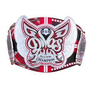 Pode incluir: Um cinturão de campeonato WWE Divas com uma placa central prateada com detalhes em cristais vermelhos, motivos de asas estilizados e o texto "DIVAS" e "BELLA TWINS CHAMPION". A correia apresenta um padrão xadrez vermelho e preto com listras brancas.