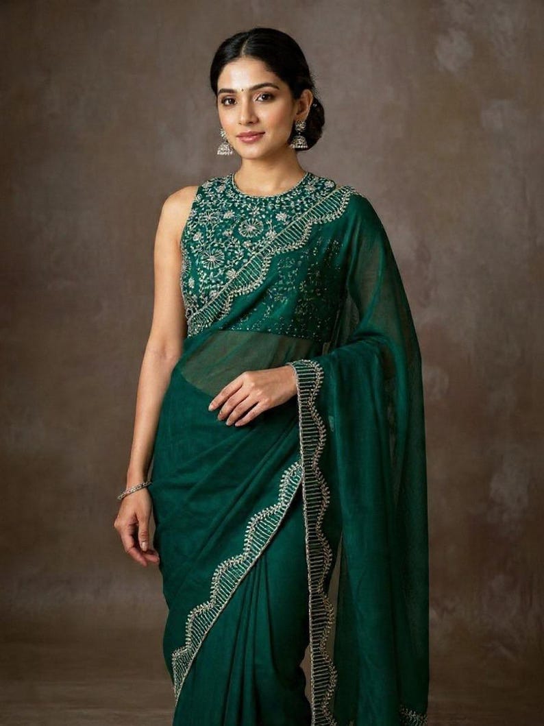 May include: A dark emerald green saree with intricate silver embroidery along the borders and neckline. The sleeveless blouse features detailed silver embellishments. The saree is draped elegantly, showcasing the flowing fabric and design.