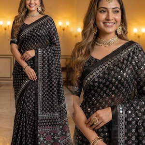 May include: Black saree with a repeating pattern of small, silver-colored dots. The saree features a decorative border with mirrored accents and a contrasting floral design in shades of pink and teal. The model is wearing gold jewelry.
