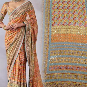 May include: A detailed saree in orange, yellow, and blue hues. The fabric is decorated with intricate patterns and embellishments. The saree is paired with a matching long-sleeved blouse with a low neckline. The design includes a border with a light blue trim.