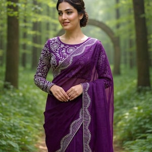May include: A woman wearing a deep purple saree with intricate silver embroidery. The long-sleeved blouse features detailed floral patterns, and the saree's border is embellished with vertical silver lines. The background is a lush green forest.