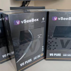 May include: Several black V6 PLUS media player boxes are displayed. Each box features the "V vSeeBox" logo in purple and white, along with the product name and a graphic of the device. The boxes are stacked, suggesting a retail or storage setting.