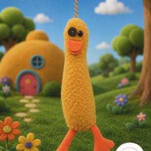May include: A yellow plush duck keyring with black button eyes and an orange beak and feet. The keyring is attached to a gold ring and chain. The background shows a whimsical outdoor scene with flowers and a cartoon house.