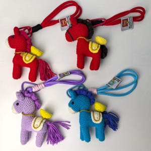 May include: Crocheted horse keychains in red, purple, and blue. Each horse has a yellow saddle, a tassel tail, and a lanyard. The keychains are handmade and feature a detailed design, perfect for adding a touch of whimsy to your keys or bag.