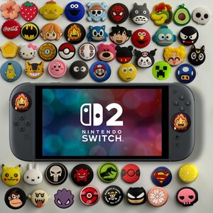 May include: A black handheld gaming console with a screen displaying the Nintendo Switch 2 logo, surrounded by a collection of colourful, circular silicone thumbstick caps featuring various pop culture characters, symbols, and icons.