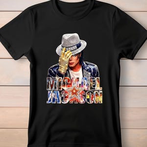 May include: Black t-shirt featuring a graphic of Michael Jackson wearing a fedora and gold glove. The shirt has the text "MICHAEL JACKSON" in a colorful, stylized font with a star in the center.