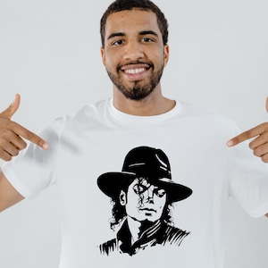 May include: White t-shirt featuring a black and white illustration of Michael Jackson wearing a hat. The image is a stylized portrait. The person in the image is pointing at the shirt.