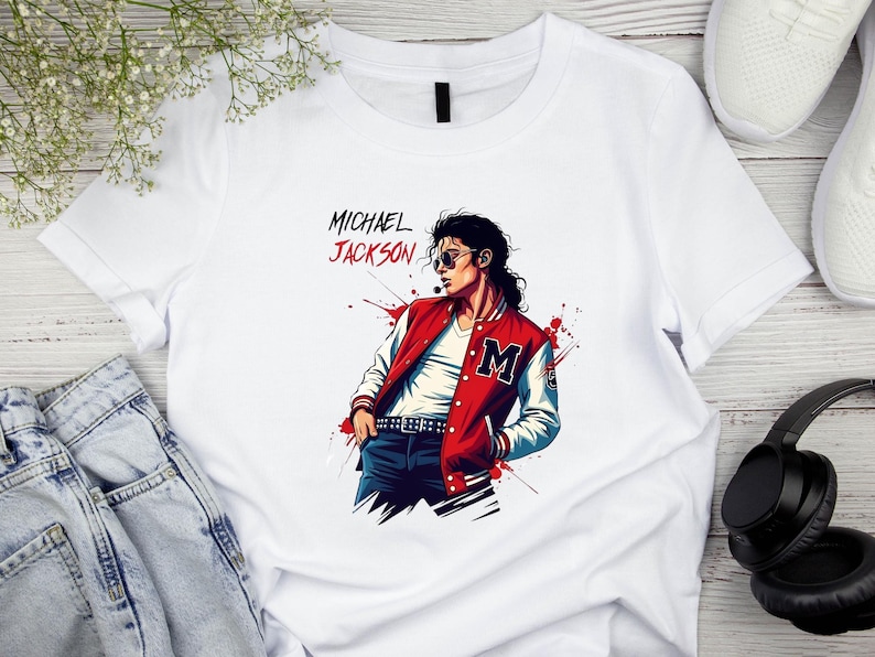 May include: White t-shirt featuring a stylized illustration of Michael Jackson in a red and white jacket with the letter "M". The text "MICHAEL JACKSON" is above the illustration in red and black.