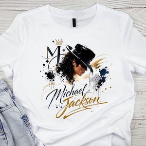 May include: White t-shirt featuring a graphic of Michael Jackson in profile, wearing a black hat and white glove. The design includes the letter "M" with a crown, and the name "Michael Jackson" in gold script.