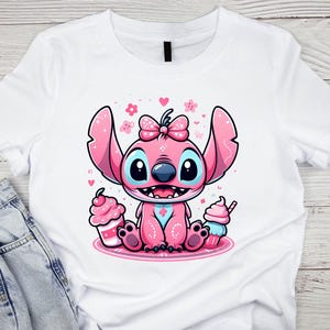 K&ouml;nnte beinhalten: Wei&szlig;es T-Shirt mit einem rosa Cartoon-Charakter-Design. Der Charakter hat gro&szlig;e Ohren, eine Schleife und blaue Augen, umgeben von Herzen und Blumen. Zwei Cupcakes flankieren die Figur. Das Design ist auf dem T-Shirt zentriert.