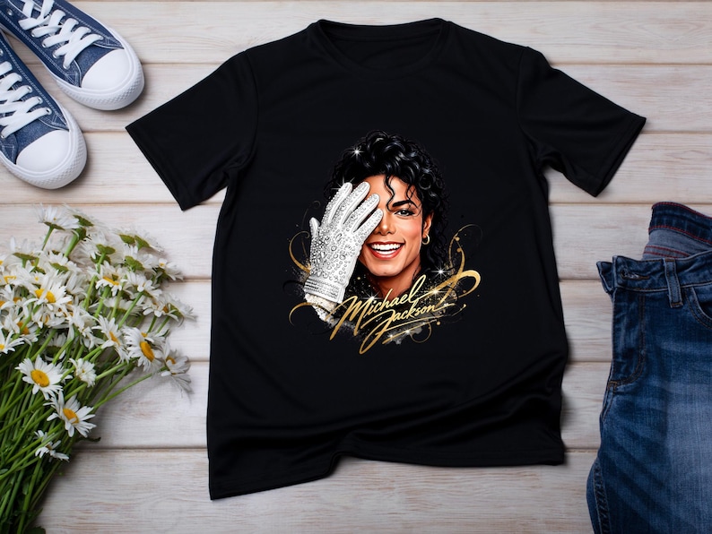 May include: Black t-shirt featuring a portrait of Michael Jackson with a white glove covering his eye. The text "Michael Jackson" is written in gold script. Blue sneakers and jeans are also visible.