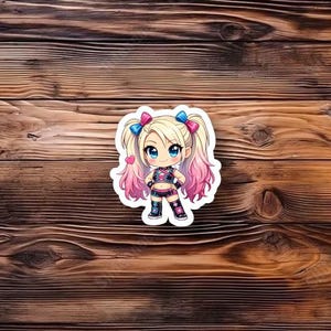 May include: A sticker featuring a cartoon character with blonde pigtails, blue eyes, and a pink and black outfit. The sticker is on a wooden background.
