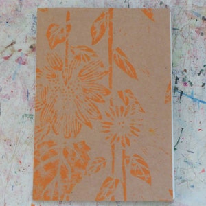 Peut inclure: Une couverture de carnet marron avec un motif floral orange représentant des tournesols et des feuilles stylisés.