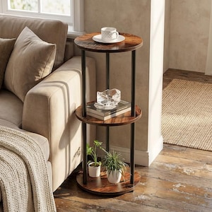 May include: A three-tiered round side table with a dark brown wood finish and black metal legs. The top shelf holds a white teacup and saucer. The middle shelf has a clear decorative object and a book. The bottom shelf displays two small potted plants.