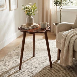 May include: A white ceramic mug with a black handle and the text "But First, Coffee" in a bold, black font. The mug is set against a blurred background, suggesting a cozy setting. The mug appears to be approximately 4 inches tall.