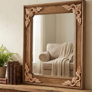 May include: A rectangular wooden mirror with ornate corner carvings. The frame is a warm brown color, and the mirror reflects a room with a beige sofa and a blanket. The mirror is displayed on a rustic wooden shelf with books and a potted plant.
