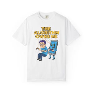 Pode incluir: Camiseta branca com um desenho animado. O gráfico apresenta uma pessoa controlada por um smartphone, com o texto "THE ALGORITHM OWNS ME" em amarelo. O design inclui linhas coloridas do arco-íris.
