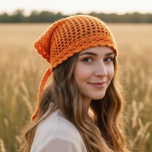 May include: An orange crochet hat with a triangular shape and a decorative edge. The hat has a loose weave design and long ties. The hat is worn by a person with long brown hair.