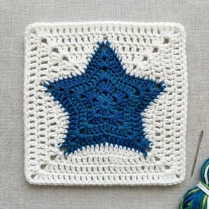 Peut inclure: Pièce carrée au crochet avec un motif d'étoile bleue sur fond blanc. L'étoile est texturée et la bordure blanche présente un motif ajouré. Un crochet et du fil sont visibles. L'article est probablement fait à la main.