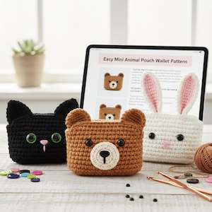 May include: Three handmade crochet animal pouches: a black cat, a brown bear, and a white bunny. The bear pouch is in the center. The bunny has pink-lined ears. A tablet displays a pattern for the pouches.