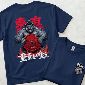 May include: Navy blue t-shirts with a graphic of a muscular sumo wrestler tearing a 25 kg weight plate. The design includes Japanese characters and flames. One shirt is folded, showing a smaller version of the graphic.