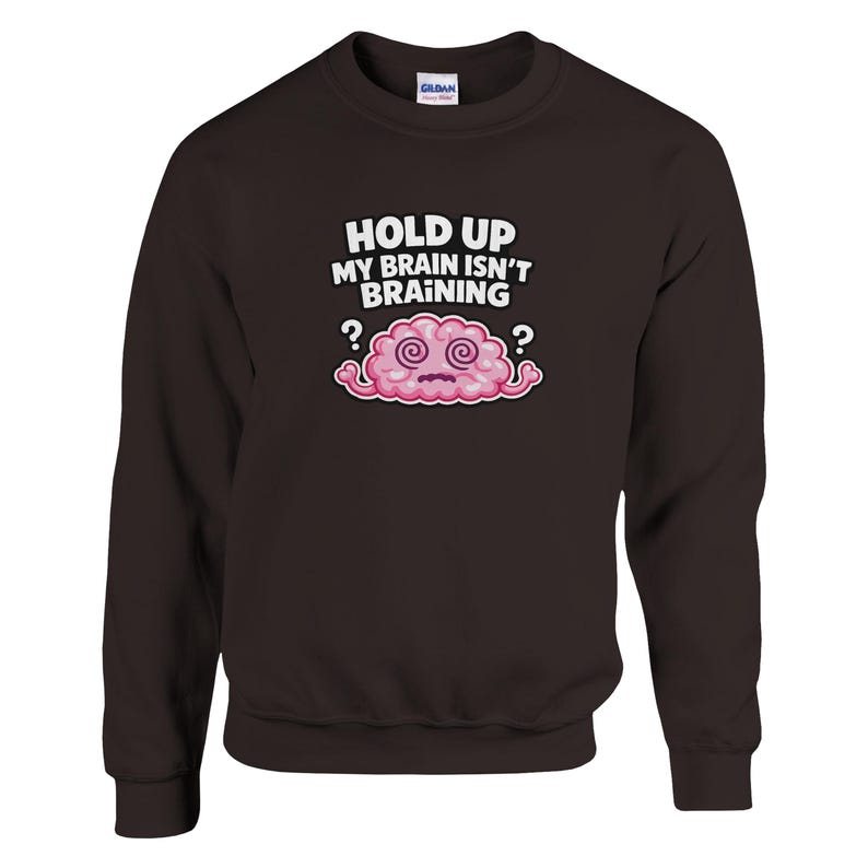 May include: A dark brown crew neck sweatshirt featuring the phrase "HOLD UP MY BRAIN ISN'T BRAINING" above a cartoon brain. The brain is pink with swirling eyes and question marks. The sweatshirt is a casual style.