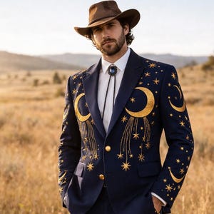 May include: Navy blue suit with gold celestial embroidery, including moons and stars. The suit features a matching jacket and pants, and is paired with a brown cowboy hat and boots. The suit has a unique, eye-catching design.
