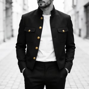 May include: A black military-style jacket with a high mandarin collar and gold-toned buttons. The jacket features two chest pockets with buttoned flaps and is worn over a plain white t-shirt, paired with matching black trousers.