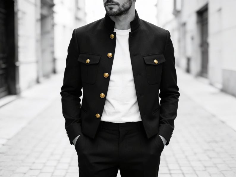 May include: A black military-style jacket with a high mandarin collar and gold-toned buttons. The jacket features two chest pockets with buttoned flaps and is worn over a plain white t-shirt, paired with matching black trousers.