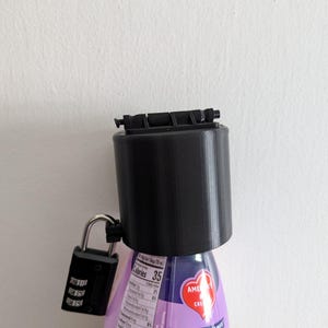 May include: A black plastic bottle cap with a combination lock attached to a purple and white bottle of coffee creamer. The creamer bottle has a label with nutritional information and the text "COFFEE'S PERFECT MATE".