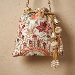 May include: A white embroidered drawstring bag with floral patterns in red, gold, and peach. It has a gold drawstring and decorative tassels with pearl beads. The bag is an elegant accessory.