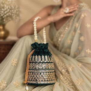 Può includere: Una borsa a sacchetto in velluto verde scuro con intricati ricami di paillettes dorate in motivi floreali e geometrici. La borsa presenta un manico di perle bianche e una coulisse dorata rifinita con una singola perla pendente.