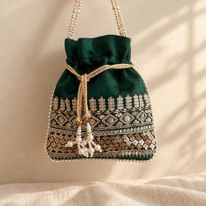 May include: A dark green drawstring pouch bag featuring gold metallic embroidery, sequins, and white faux pearl bead trim. The bag includes a gold braided drawstring cord with dangling pearl tassels and a double-strand pearl bead handle.