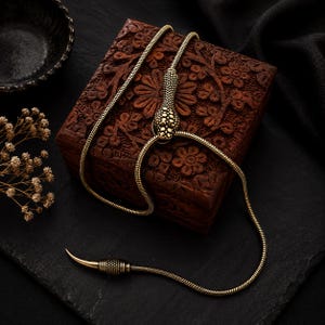 May include: A gold-toned snake-shaped lariat necklace featuring a textured serpent head and a pointed tail end. The flexible chain is designed to loop through the snake head, allowing for adjustable length and a secure fit around the neck.